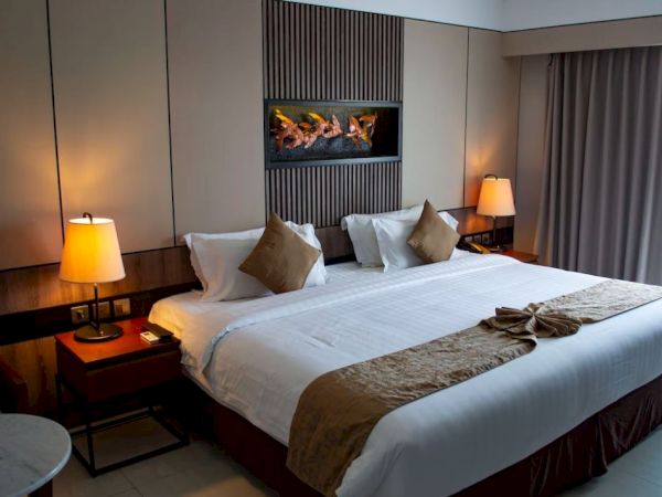 A stylish hotel room with a large bed, decorative pillows, bedside lamps, a wall decoration, curtains, and a small table.