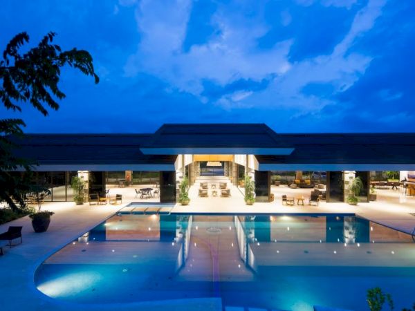 A luxurious, illuminated poolside area of a modern building at twilight, with a serene ambiance and stylish outdoor seating.