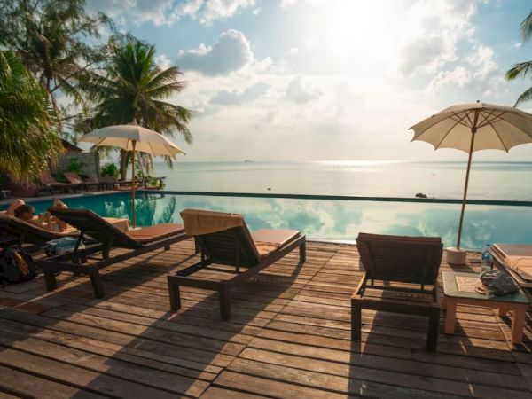 A serene beach scene with lounge chairs, umbrellas, palm trees, and a vibrant ocean view under a partly cloudy sky, creating a relaxing vibe.