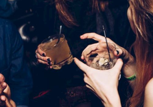 People enjoying drinks and laughing in a lively social setting, holding cocktails with straws, creating a warm and joyful atmosphere.