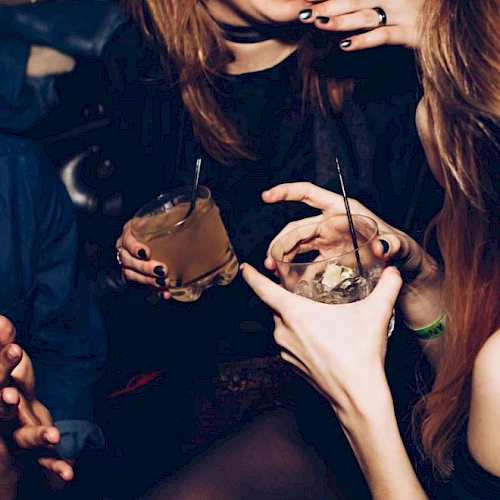 People enjoying drinks and laughing in a lively social setting, holding cocktails with straws, creating a warm and joyful atmosphere.