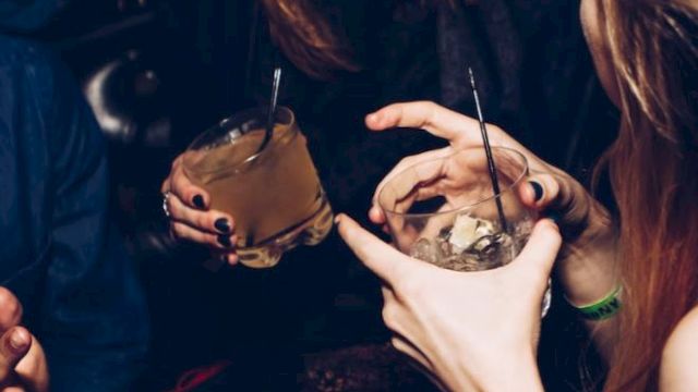 People enjoying drinks and laughing in a lively social setting, holding cocktails with straws, creating a warm and joyful atmosphere.