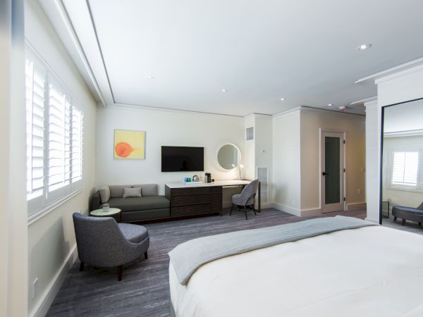 A modern hotel room with a large bed, wall-mounted TV, seating area, and mirror. Neutral tones create a calm and spacious atmosphere.