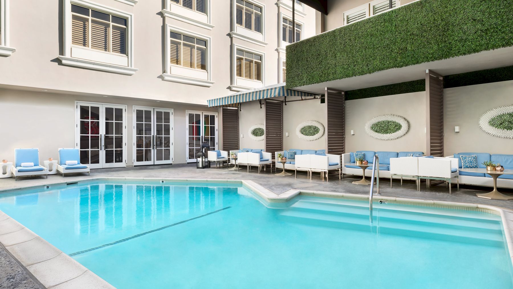 A modern poolside area with light blue cushioned seating, clean white walls, and green decor accents, perfect for relaxation and socializing.