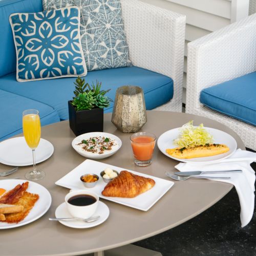 A cozy setup with a table of breakfast items, including croissants, omelette, drinks, and a sofa with blue cushions.