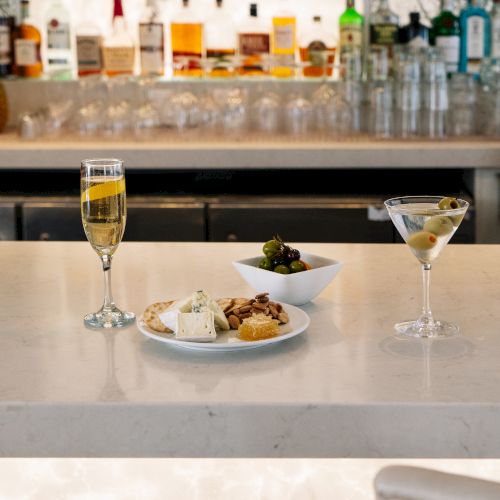 A bar counter with drinks, a cheese plate with crackers, and a bowl of olives. Bottles are visible in the background.