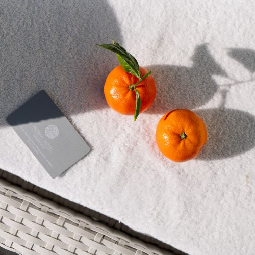 The image shows two oranges with leaves and a rectangular card on a light-colored surface, casting distinct shadows.