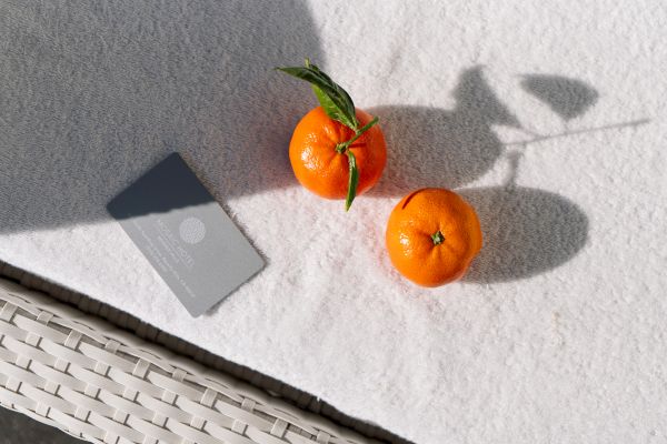 Two oranges and a hotel key card on a white textured surface, casting shadows.