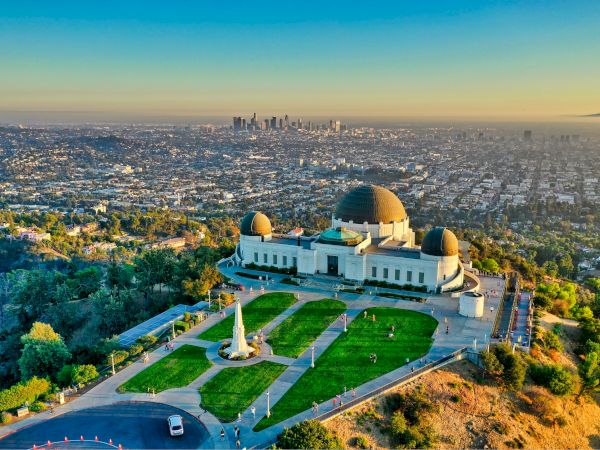 The image shows an aerial view of an observatory with a cityscape in the background during sunset.