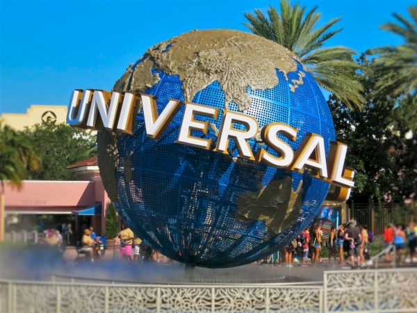 The image shows a large globe with "UNIVERSAL" written on it, surrounded by people and palm trees in a theme park setting.