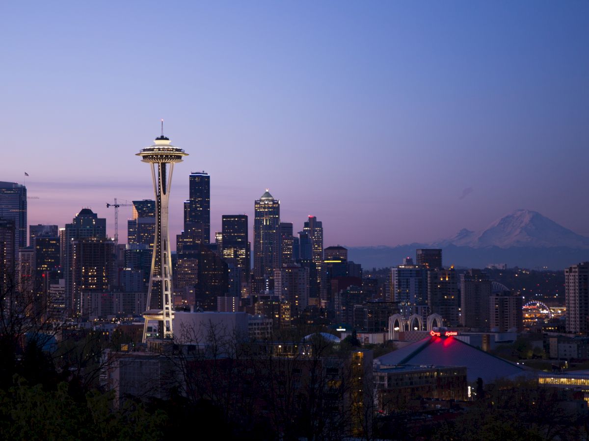 A city skyline at dusk with the Space Needle, other buildings, and a distant mountain under a twilight sky.